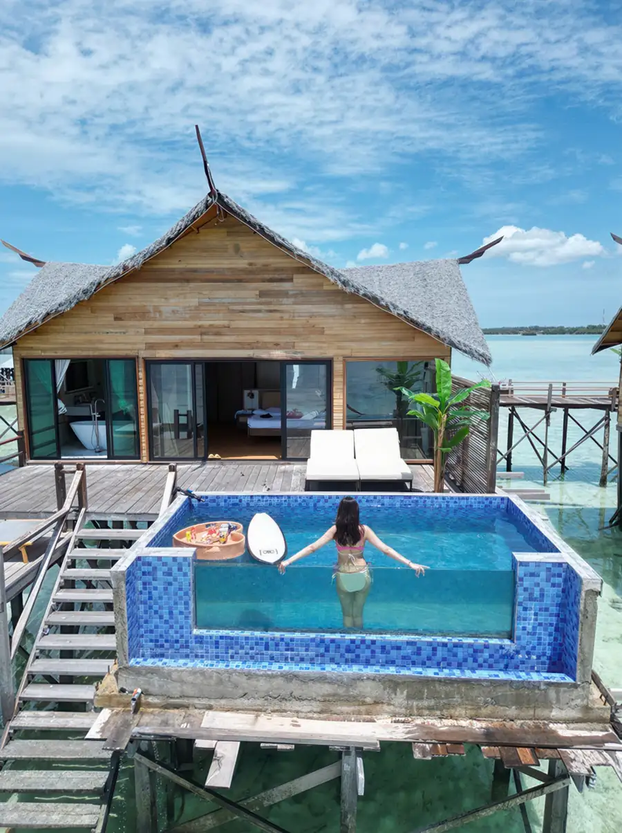 An aerial view of white overwater chalets over a vibrant reef, featuring private swimming pools, white mesh bed nets, and direct access to the sea, built in a local style at Jelly Sea Resort.