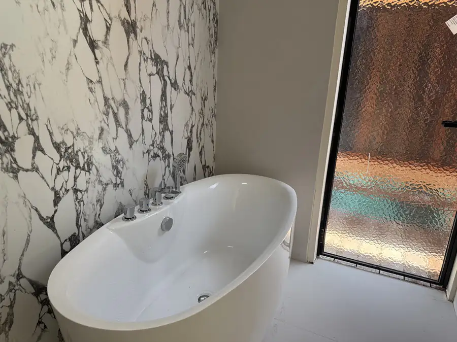 A close-up of a white freestanding bathtub with chrome control knobs and a hand shower set against a black-and-white marble-effect wall at Jelly Sea Resort.