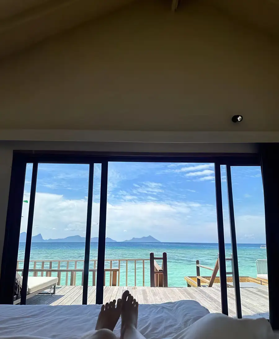 A beautiful bedroom at Jelly Sea Resort near Semporna showing a bed with towel art facing folding glass doors opening onto the balcony with seaviews, elegant light wood floors, and air conditioning.
