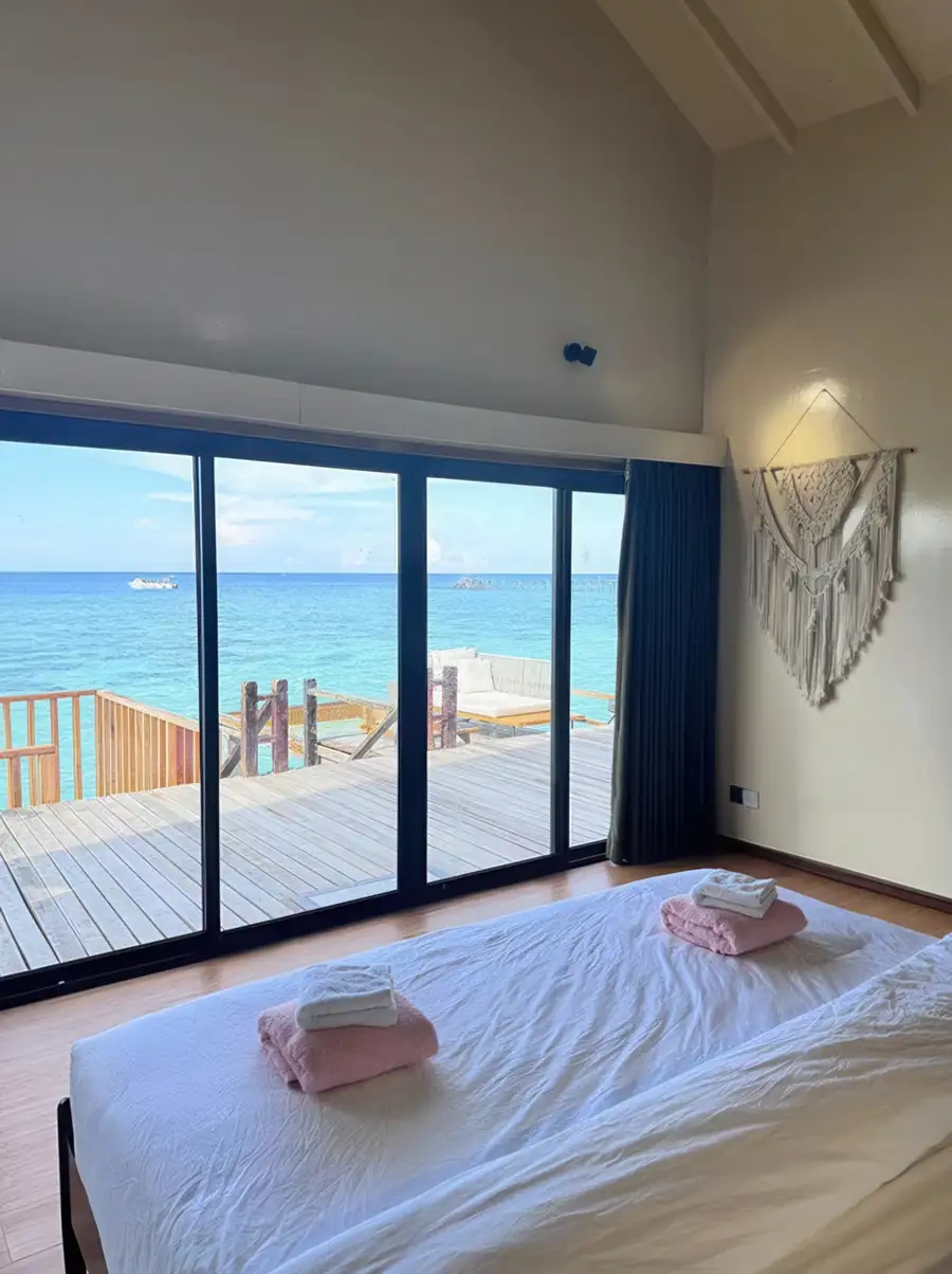 A comfortable bedroom at Jelly Sea Resort in the Celebes Sea focusing on a cozy bed with swan towel art, facing large glass doors opening onto the balcony, polished teak wood floors, and AC.