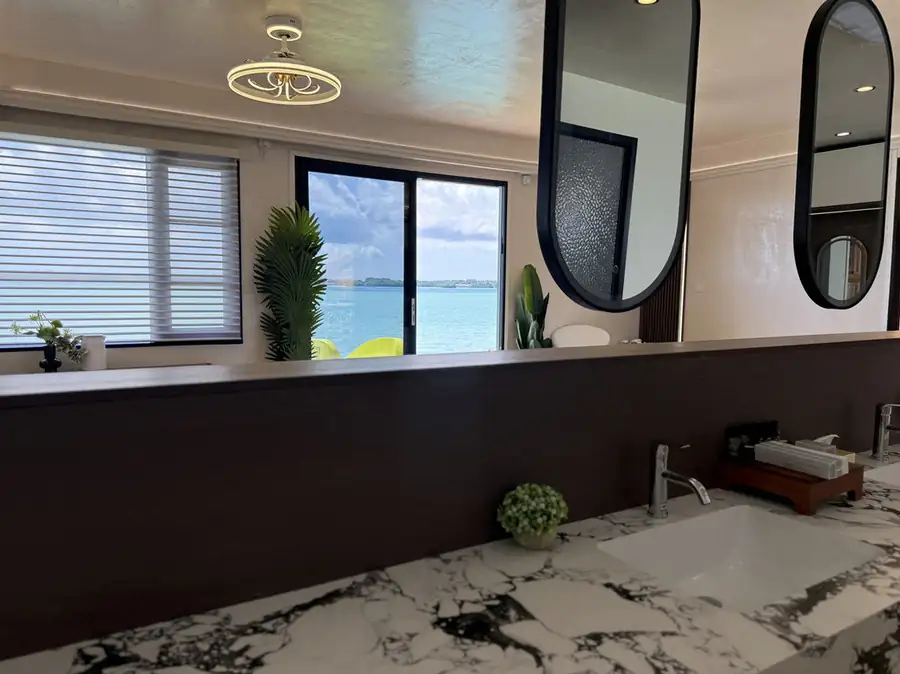 A practical bathroom layout at Jelly Sea Resort displaying a modern white ceramic toilet next to a light wood vanity, tiled floors, and a glass-enclosed electric shower.