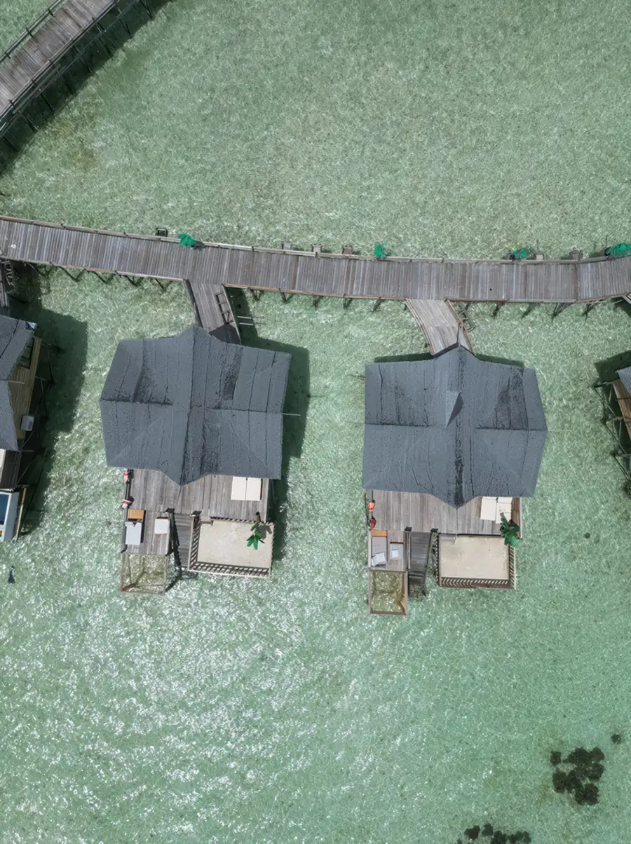 A close aerial perspective of white overwater chalets featuring private balconies and overwater hammocks, showcasing traditional vernacular styling at Jelly Sea Resort.