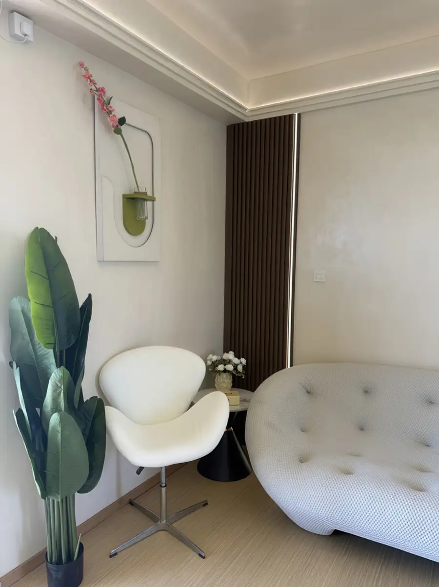A stylish bedroom at Jelly Sea Resort near Semporna showcasing a designer tufted sofa and modern white swivel chair over smooth wooden boards, AC.