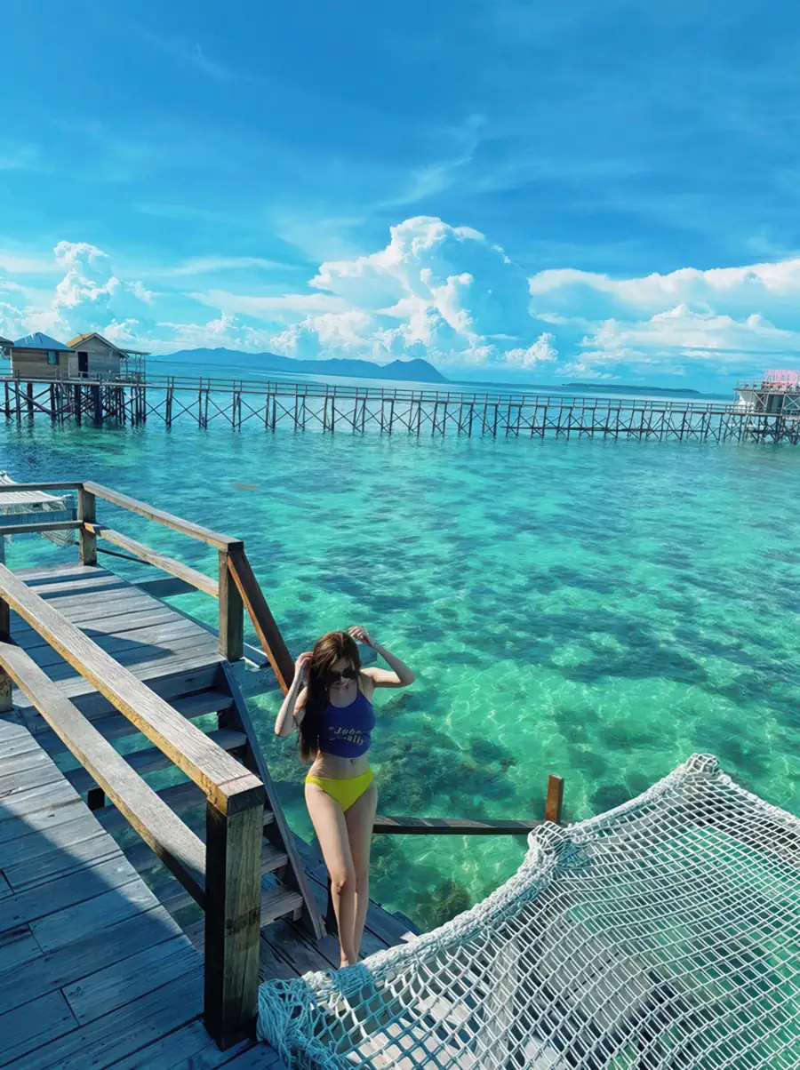 Private sunlit balcony featuring a suspended mesh deck and hanging chair at Jelly Sea Resort. Enjoy an unforgettable experience with a cool tropical breeze while suspended over the pristine Semporna waters.