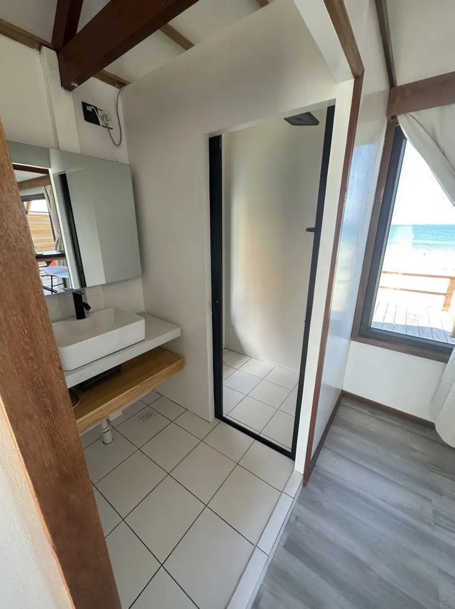A spacious bathroom at Jelly Sea Resort showcasing a beautiful light wood double vanity, two backlit round mirrors, white washbasins, and an electric shower.
