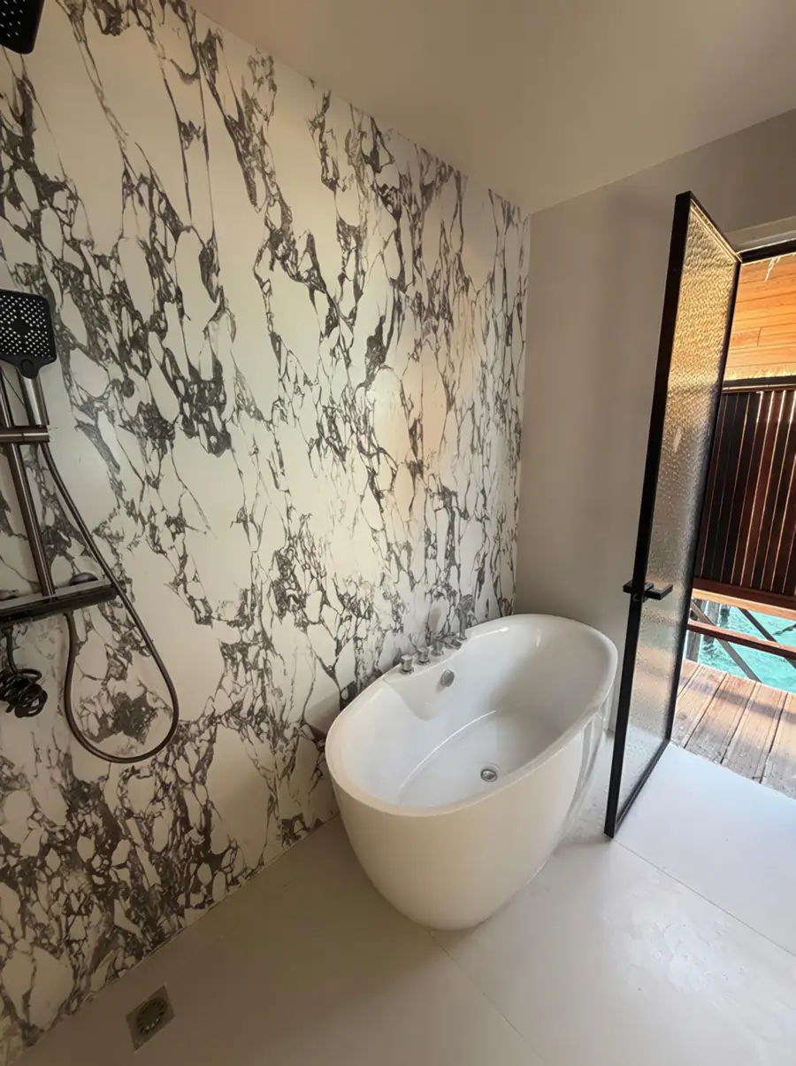 A contemporary bathroom featuring a freestanding white tub and marble-patterned tiling with a view through an open glass door to the sea at Jelly Sea Resort.