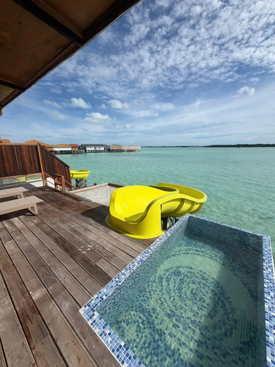 Private sunlit balcony featuring a glass plunge pool, an overwater slide and a suspended mesh bed at Jelly Sea Resort. The perfect water resort for sea turtle spotting in Tun Sakaran Marine Park.
