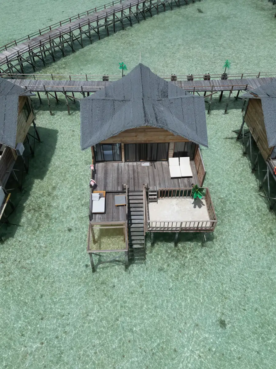A high-altitude drone view revealing white overwater chalets with private balconies connected by a curved boardwalk, inspired by traditional island village layouts at Jelly Sea Resort.