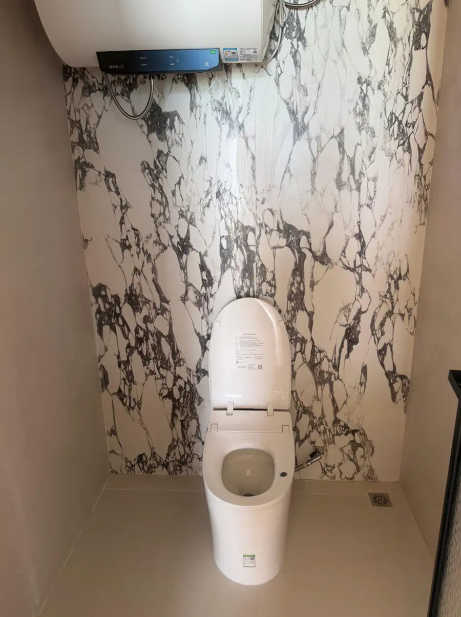 A stylish vanity area at Jelly Sea Resort showcasing a round backlit mirror, a pristine white washbasin, pump toiletry bottles, elegant slatted wood wall details, and an electric shower.