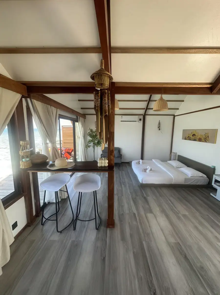 A bright bedroom at Jelly Sea Resort near the Celebes Sea showcasing a large bed, white bar stools, and grey wood-textured floors, all kept cool by a/c.
