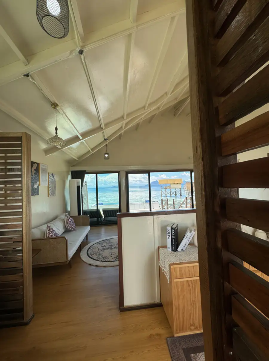 A stylish bedroom at Jelly Sea Resort near Semporna featuring a cane-sided sofa, vaulted ceilings, and rustic timber floor with smooth wooden boards, with air con.