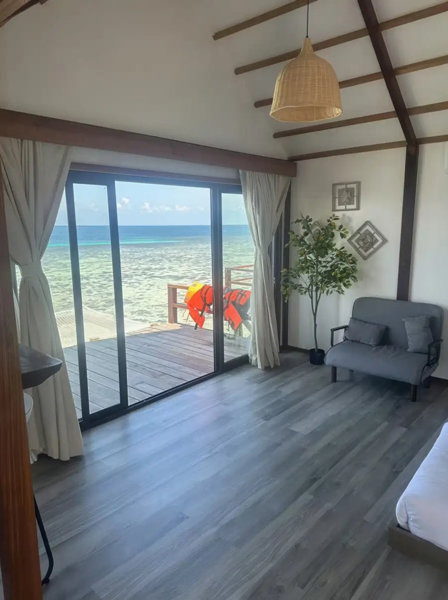 A stylish room at Jelly Sea Resort near Bum Bum Island with a grey sofa by panoramic glass doors opening onto the private balcony with seaviews and aircon.