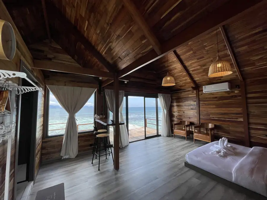 A luxury room at Jelly Sea Resort near Semporna where the bed faces panoramic glass doors opening onto the private balcony with seaviews, featuring air con and timber walls.