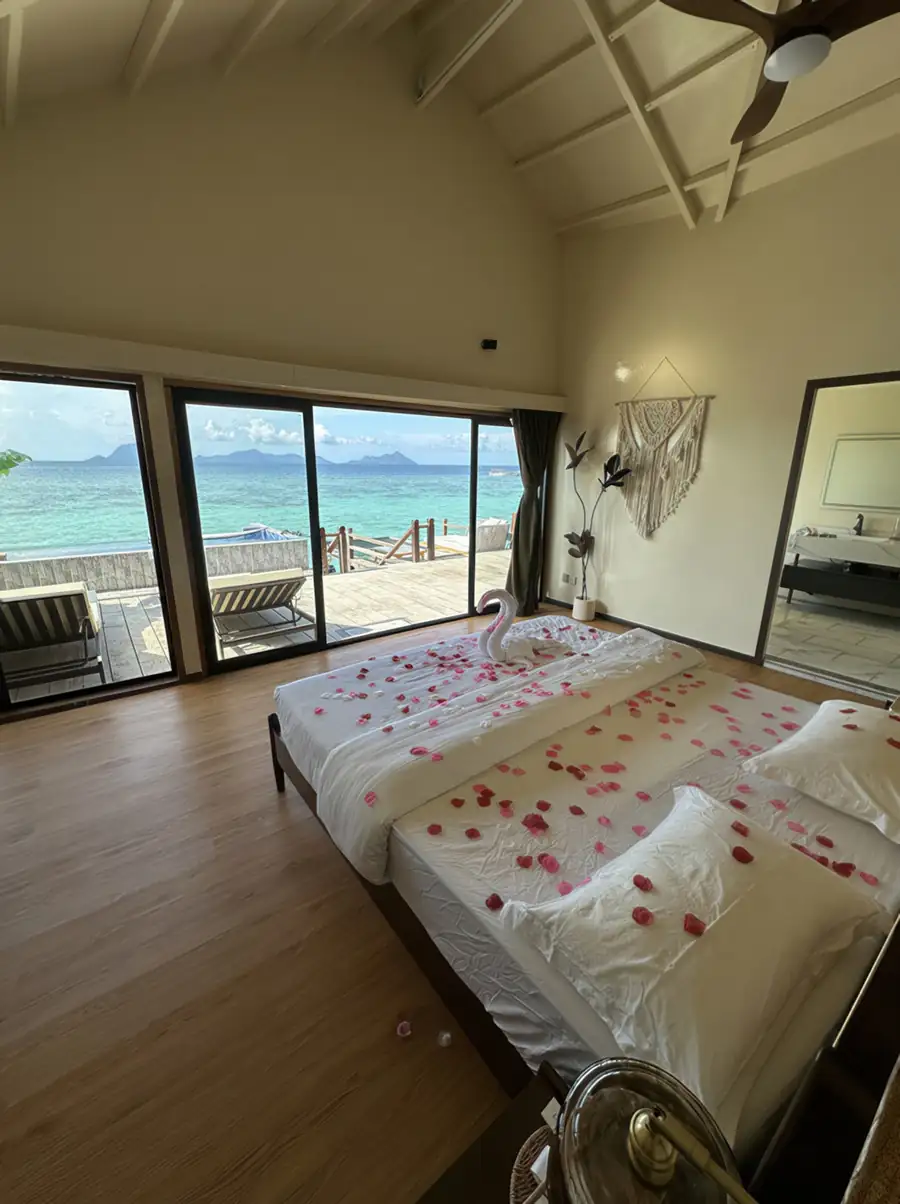 A romantic bedroom at Jelly Sea Resort in the Celebes Sea with a rose petal-strewn bed facing panoramic glass doors opening onto the balcony with seaviews, featuring a/c.