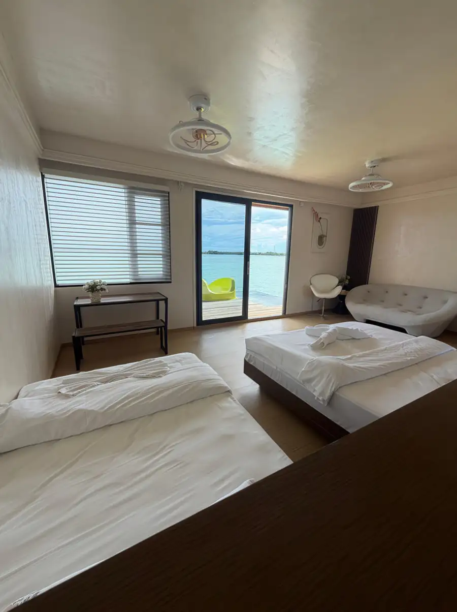 A massive bedroom at Jelly Sea Resort in the Celebes Sea featuring two large beds, a curved sofa, and warm wooden plank floor with varnished timber flooring, cooled by air conditioning.