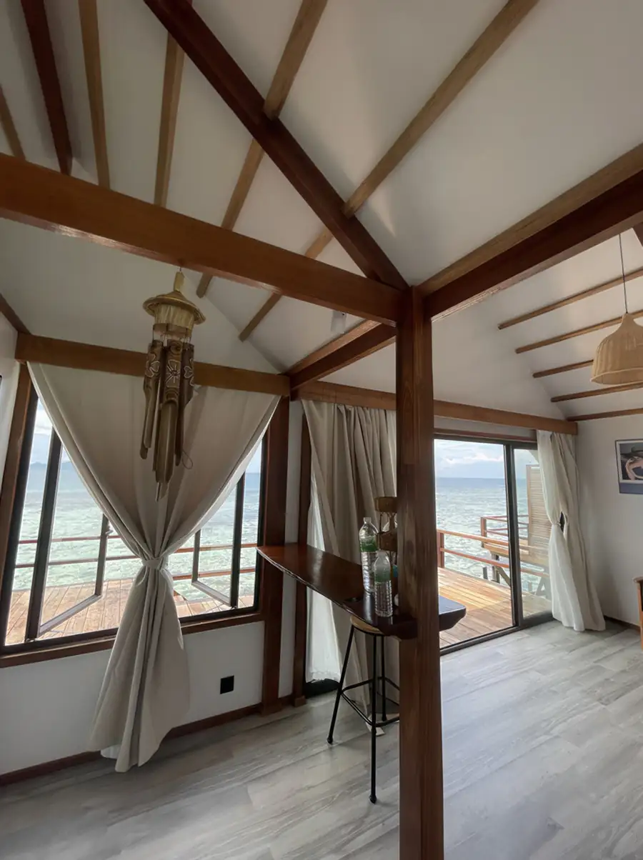 A bright room at Jelly Sea Resort near the Celebes Sea with high vaulted ceilings, a wooden bar, and grey wood-textured floors, cooled by an air con unit.