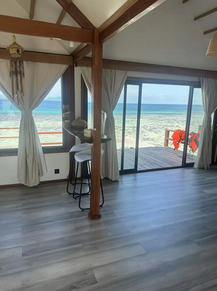 A bright room at Jelly Sea Resort near Semporna with a wooden breakfast bar facing large glass doors, grey wood-textured floors, and a/c for a cool stay.