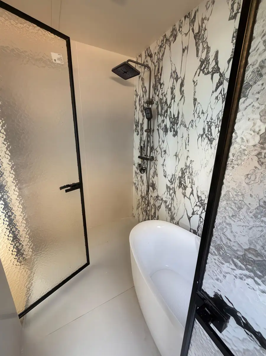 A modern bathroom featuring a white freestanding tub against a bold black-and-white marble-patterned accent wall with an overhead rain shower at Jelly Sea Resort.