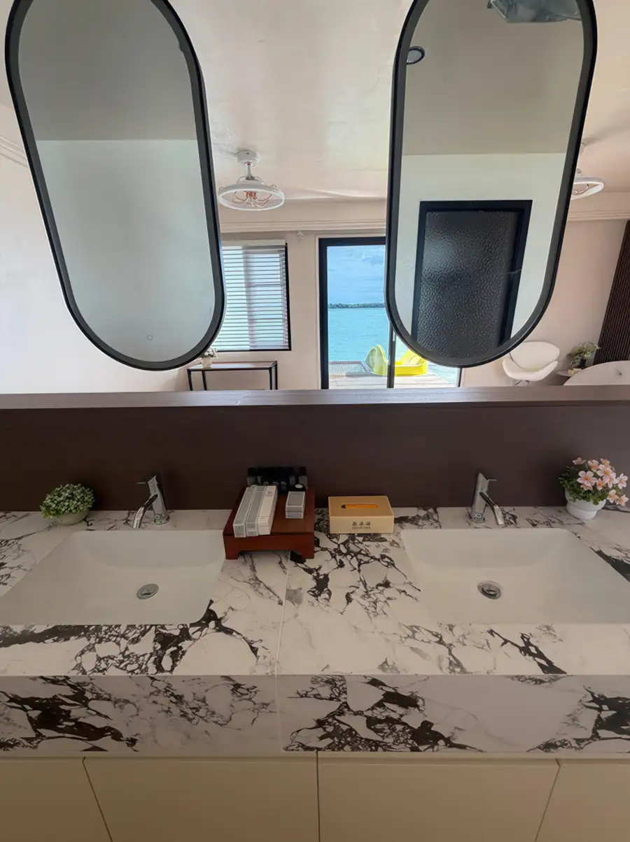 A modern open concept bathroom at Jelly Sea Resort featuring a light wood vanity, a backlit round mirror, a modern washbasin, a white toilet, and an electric shower.
