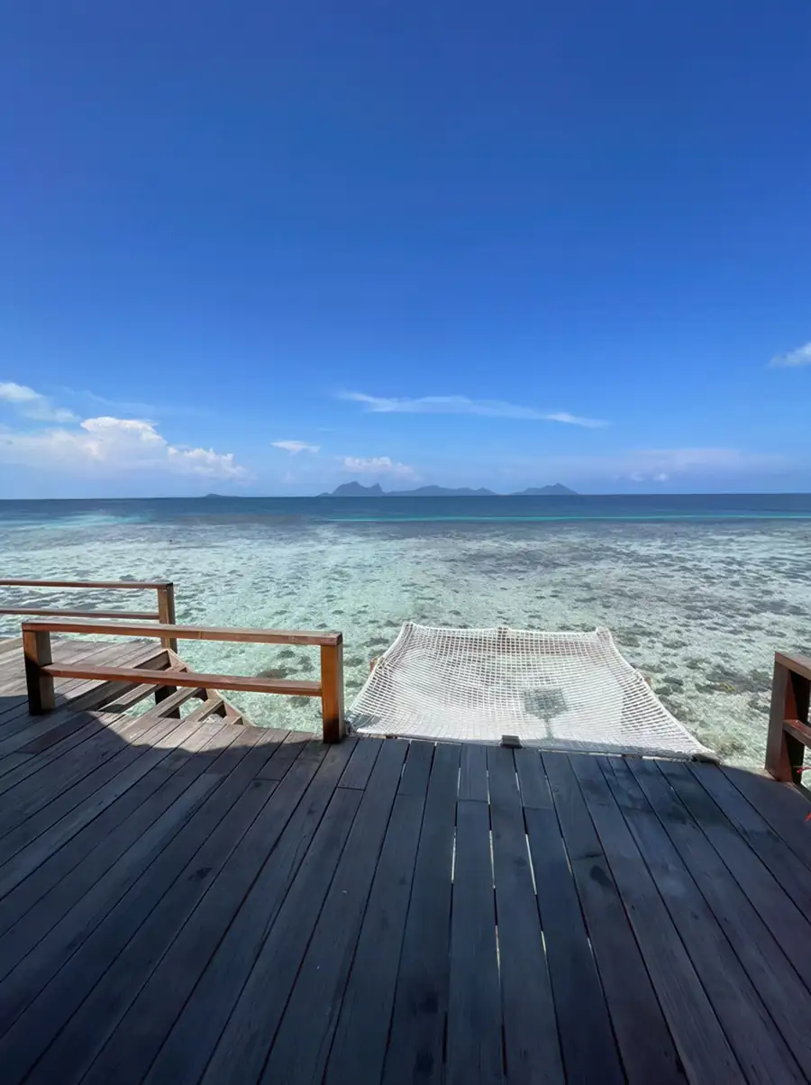 Private sunlit balcony featuring a clean catamaran-style net lounge at Jelly Sea Resort. An intimate over the water escape offering stunning views toward the islands of Pulau Bohey Dulang.