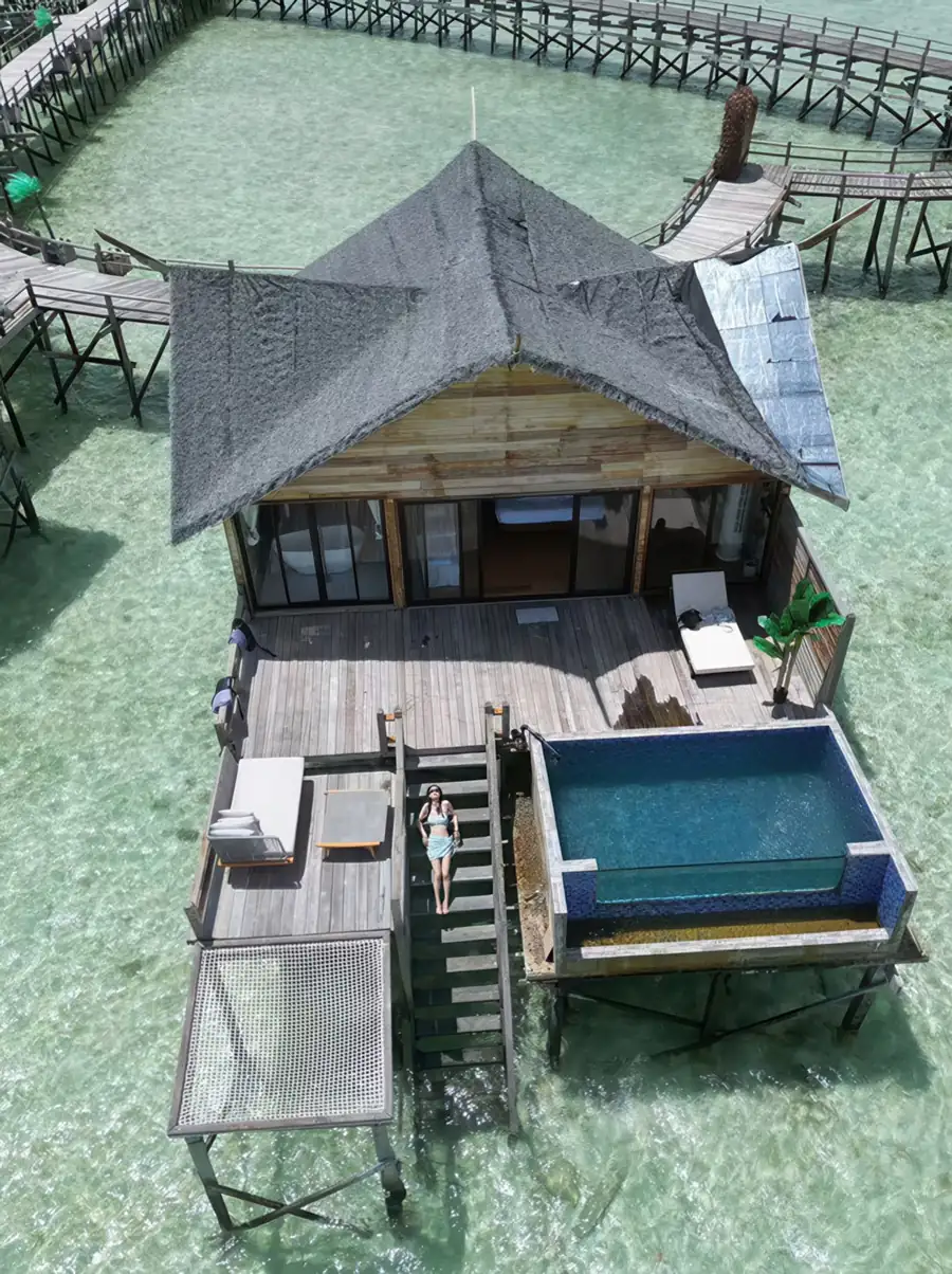 A private wooden deck extending over the water, equipped with a white mesh bed net, lounge chairs, and direct access to the sea, showcasing a traditional Sabah style at Jelly Sea Resort.