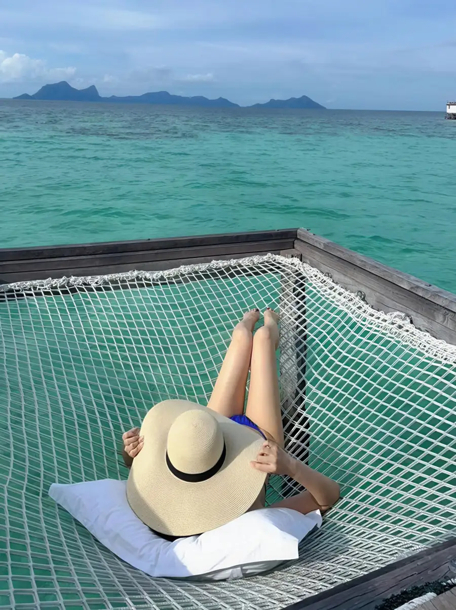 Guest on a suspended overwater hammock net at Jelly Sea Resort. This floating paradise in the Semporna Archipelago suspends guests between sea and sky above crystal-clear waters.