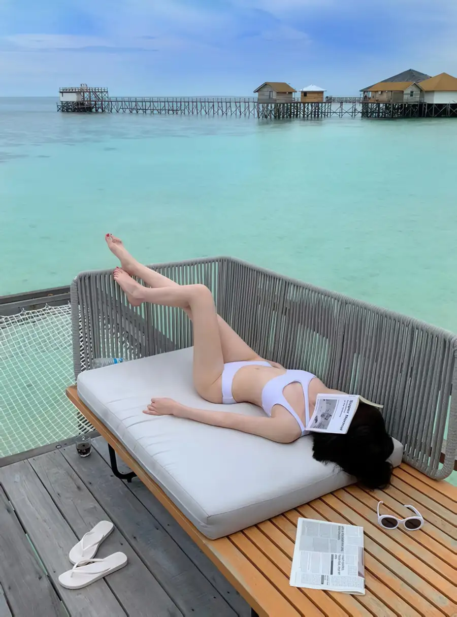 A guest relaxing with a book on a comfortable daybed on a private overwater balcony at Jelly Sea Resort, an intimate over the water escape enjoying the gentle sea breeze of Semporna archipelago.
