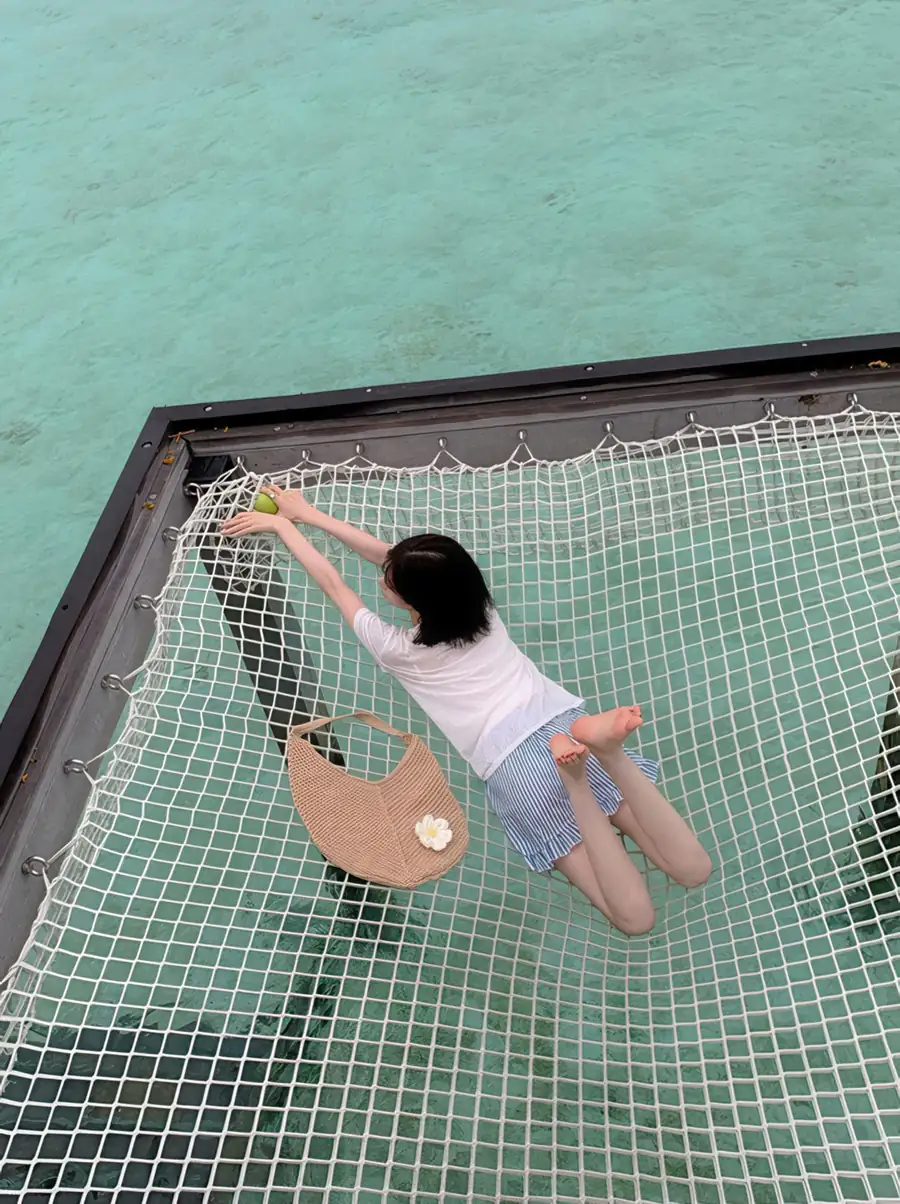 Guest relaxing on a suspended catamaran-style net lounge at Jelly Sea Resort. Enjoy barefoot luxury and a cool tropical breeze above the vibrant Semporna marine sanctuary.