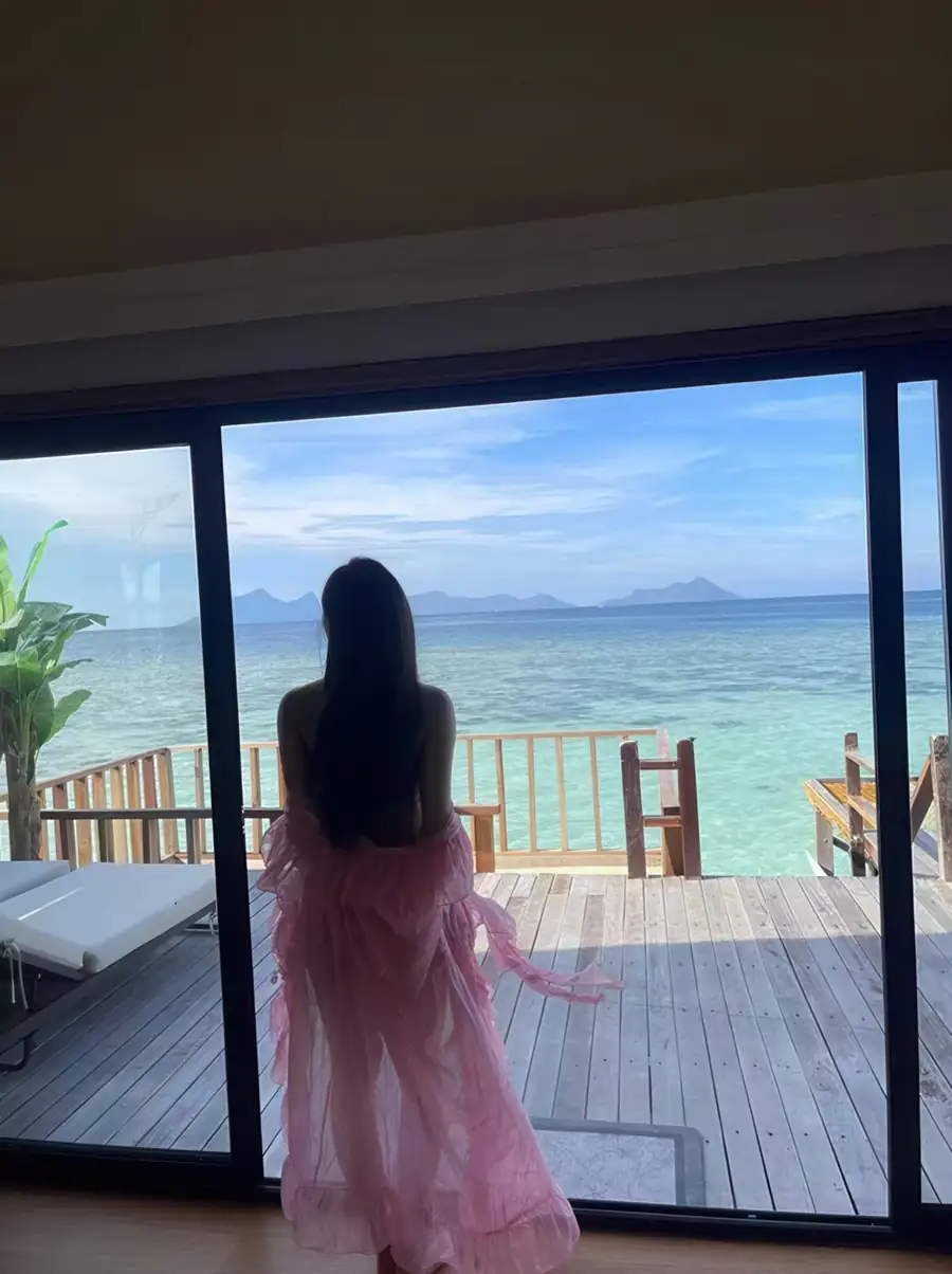 A guest gazing out from an open sliding door onto a private outdoor deck with sea views at Jelly Sea Resort, a romantic over water haven near the islands of Tun Sakaran Marine Park.