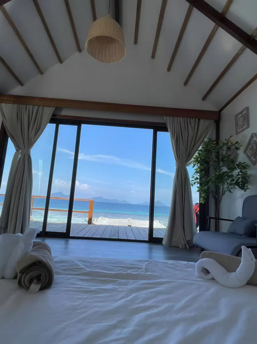 An elegant bedroom at Jelly Sea Resort in the Celebes Sea detailing a large king bed with intricate swan towel art and rose petals, a wooden headboard, authentic glossy hardwood floors, and A/C.