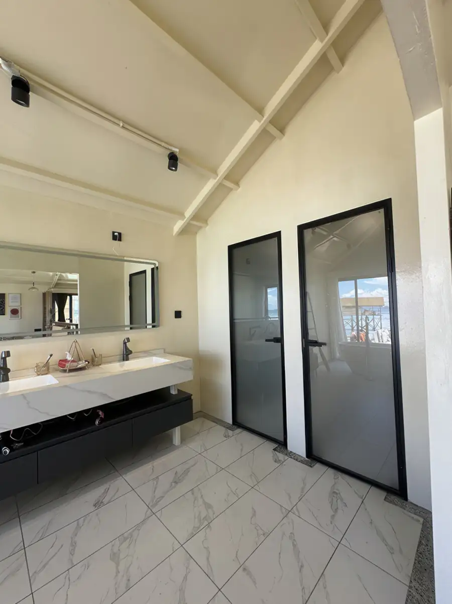 A beautifully designed bathroom at Jelly Sea Resort detailing an open plan layout with a light wood vanity, an illuminated round mirror, a sleek washbasin, and an electric shower.