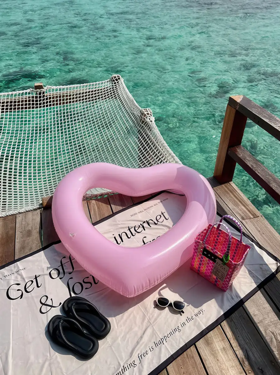 A pink heart float and beach bag resting next to a private overwater mesh bed at Jelly Sea Resort. Prepare for a relaxing midday nap in the sun at this breathtaking Semporna getaway.